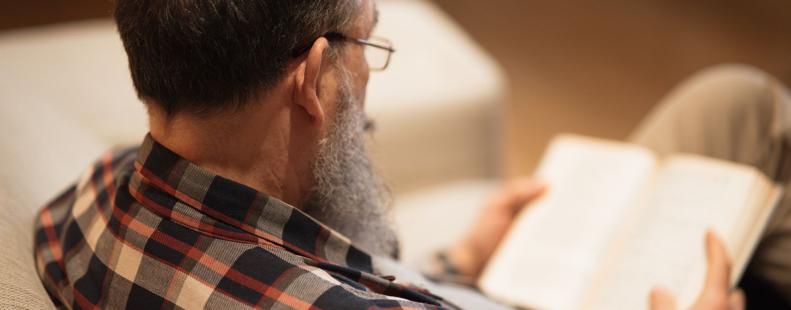 An older man in reading glasses going through a printed booklet at home, the way most people meet a Medicare Advantage Summary of Benefits during Annual Enrollment
