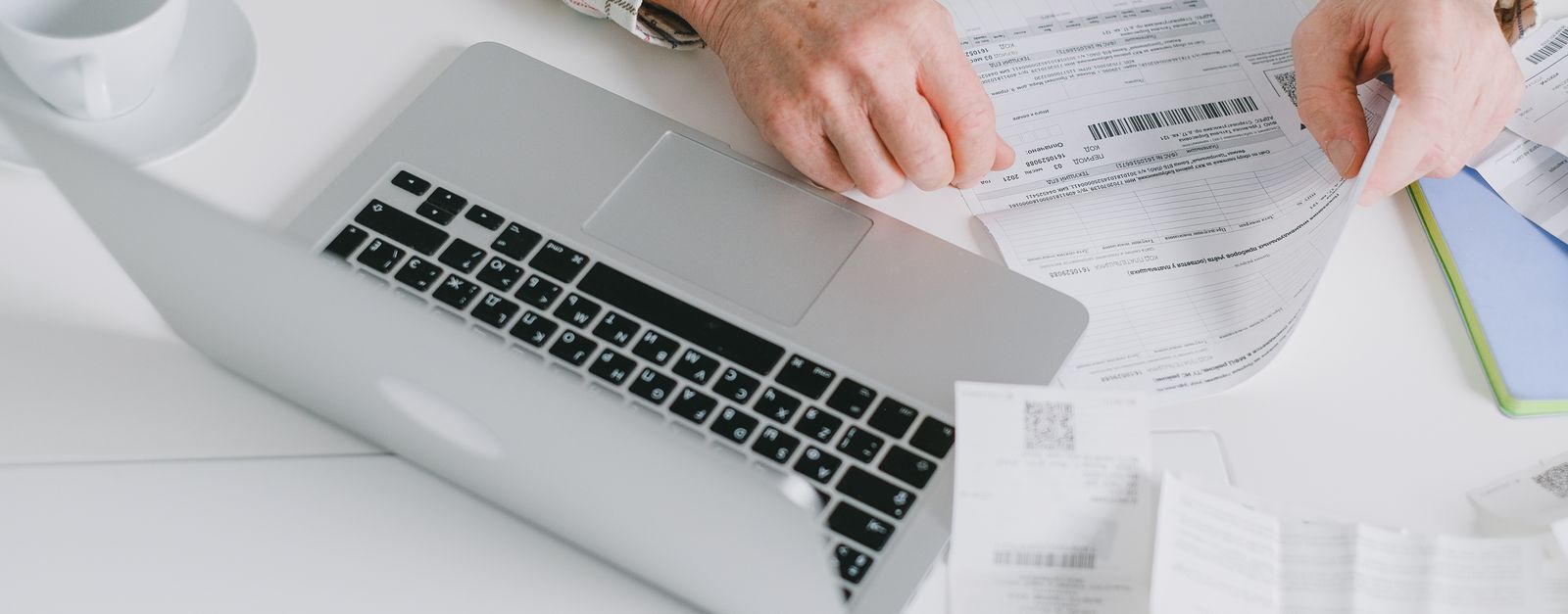 An older man's hands at a laptop beside printed statements, working through Medicare Plan Finder to compare 2027 plans after a Presbyterian plan non-renewal