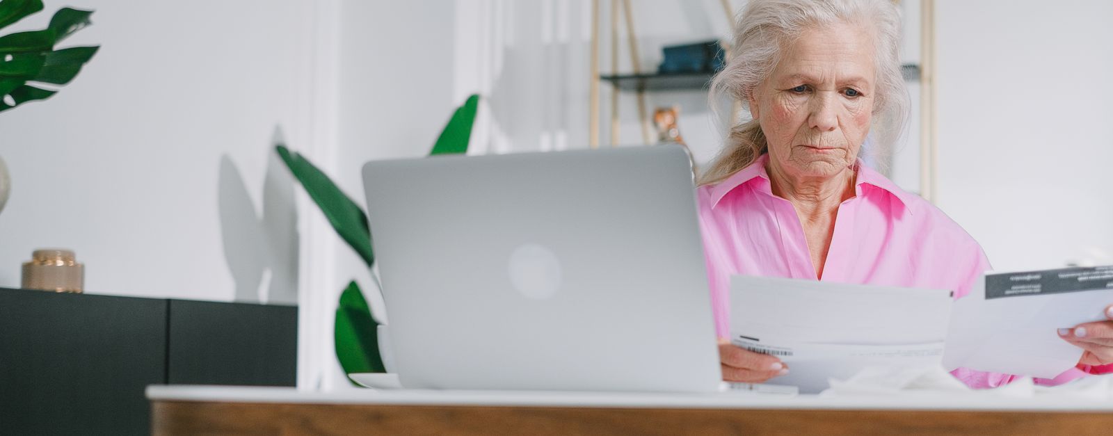 An older woman reads a letter at her desk beside a laptop — a New Mexico Medicare Advantage member reviewing the 2027 Annual Notice of Change that explains why her premium, copays and drug tiers moved