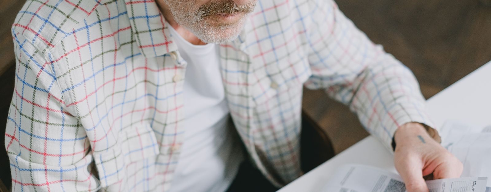 An older man in reading glasses studies an official letter at his table — Blue Cross and Blue Shield of New Mexico Medicare Advantage members received non-renewal notices for 2027 in early October