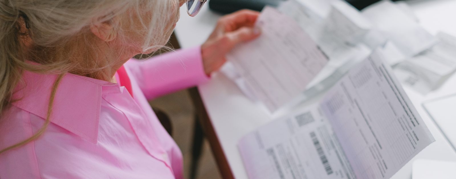 An older woman in glasses holding two printed pages side by side at a table, comparing the Medicare Advantage plans available in Albuquerque for 2027